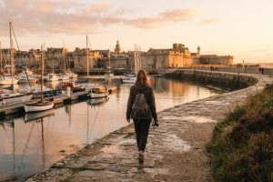 Promeneuse face au port fortifié de Saint-Malo au coucher du soleil